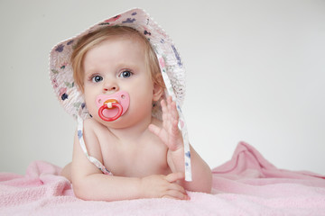 Studio portrait of adorable baby girl with pacifier wearing a hat
