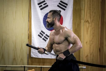Photo sur Aluminium Arts martiaux Hombre fuerte con grandes músculos entrenando artes marciales con katana. Defensa personal con espada.