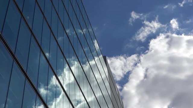 Fluffy white clouds on blue sky mirrored in modern glass building