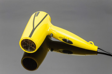 Yellow foldable hair dryer on the grey mirror background