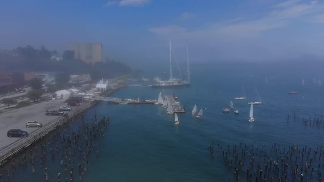 A laterally-moving aerial view over the sailboats, boats, and piers at Portland, Maine's eastern promenade on a foggy summer day.  	