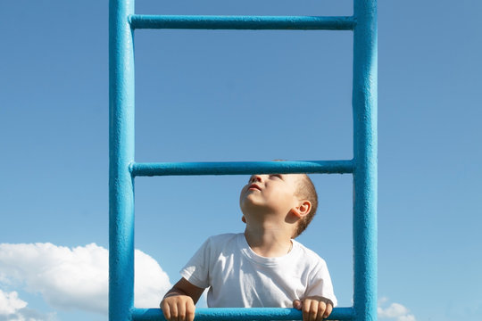 The blond boy climbs the stairs on the playground and looks up.