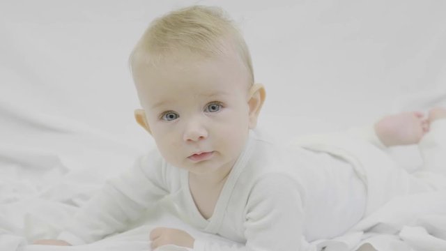 Blond baby with blue eyes lye on bed and look at camera, hypnotize look, lethal charm