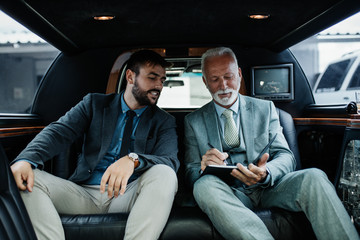 Senior businessman and his assistant sitting in limousine and working together. - obrazy, fototapety, plakaty