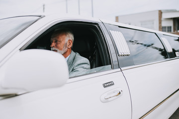 Senior good looking limousine driver driving white luxury limousine.