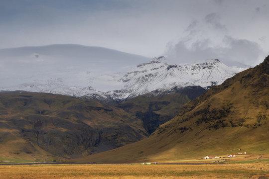 Landscape in Iceland. Wild nature, mountains, houses, grass, snow and clouds