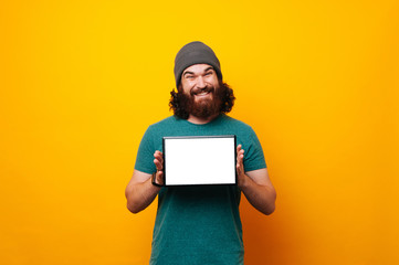 Happy young man with beard smiling and holding tablet with white empty screen