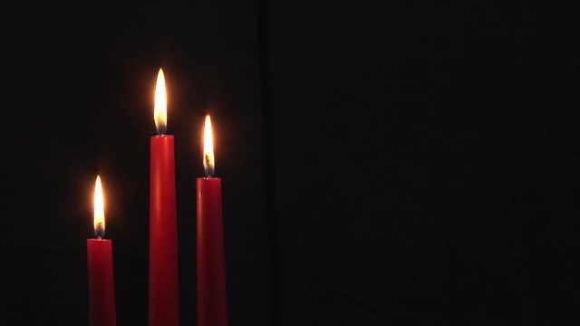 Group of three burning dark red dinner candles with black background with copy space.