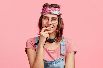 People, subculture and freedom concept. Delighted satisfied hippie woman with gentle smile, meets with friend, have pleasant talk, wears stylish bandana on head, isolated over pink background