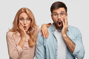 Surprised lovers doesn`t expect to notice someone in house, keep hands on cheeks, see something...