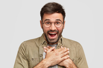Studio shot of handsome surprised glad bearded male doesn`t expect to recieve present, being...