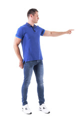 Profile of young adult caucasian man in blue polo shirt pointing finger away showing copyspace. Full body isolated on white background. 