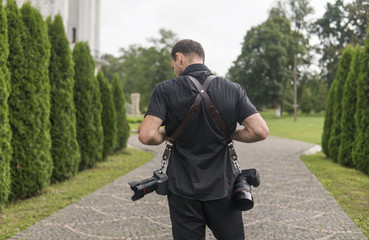 Back of professional wedding photographer in black shirt and with a two cameras an a shoulder...