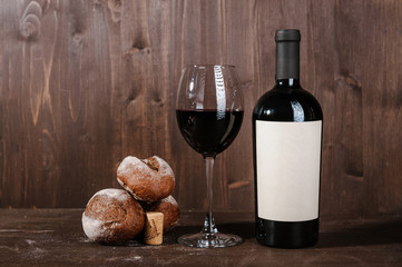 red wine composition with bread, two bottles in box and wineglass on wooden background