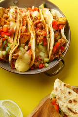 Close up of mexican tacos with chili con carnes and grated cheese served over a yellow background