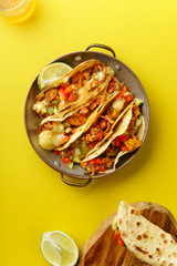 Overhead image of mexican tacos with chili con carnes and grated cheese served over a yellow background