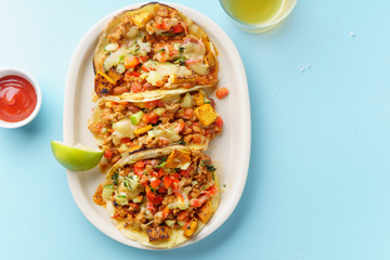 Overhead image of mexican tacos with chili con carne, sweet potatoes and grated cheese served over a blue background. Text space