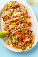 Overhead image of mexican tacos with chili con carne, sweet potatoes and grated cheese served over a blue background