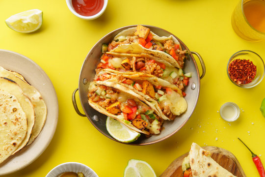 Overhead image of mexican tacos with chili con carnes and grated cheese served over a yellow background
