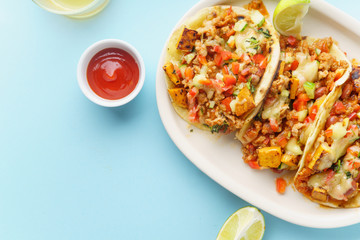 Overhead image of mexican tacos with chili con carne, sweet potatoes and grated cheese served over a blue background. Text space
