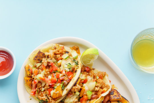 Overhead image of mexican tacos with chili con carne, sweet potatoes and grated cheese served over a blue background. Text space