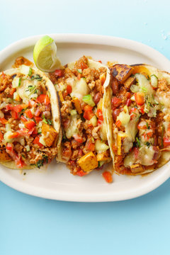 Overhead image of mexican tacos with chili con carne, sweet potatoes and grated cheese served over a blue background