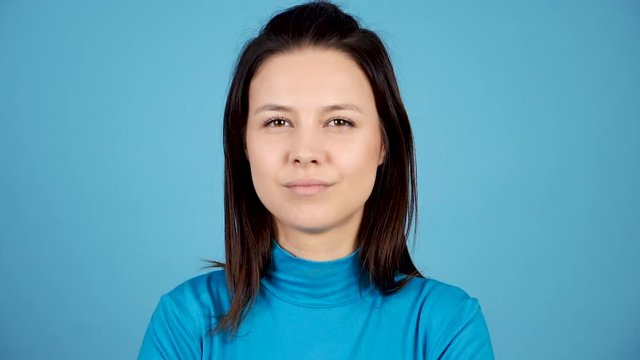 Slow motion woman smiling largely to the camera on blue background in studio. Young adult being happy