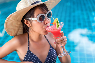 Bikini asian woman in pool relaxing drinking cocktail,juice with sunglasses, young beautiful sexy...