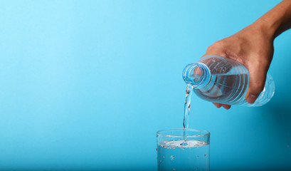 Closeup of pouring mineral water from bottle into glass by man's hand.