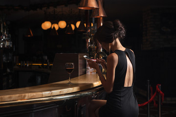 Naklejka na ściany i meble Beautiful elegant lady with a smartphone and a glass of wine in a restaurant