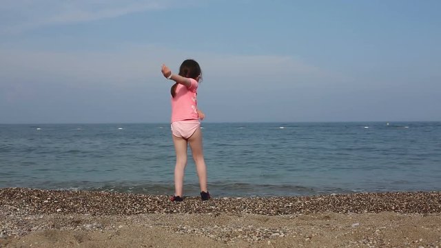 Beautiful girl dressed in a swimsuit throwing stones into the sea