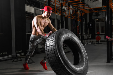 Fototapeta na wymiar Shirtless man flipping heavy tire at gym