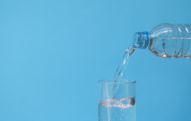 Pouring mineral drinking water from bottle into glass with blue background. 