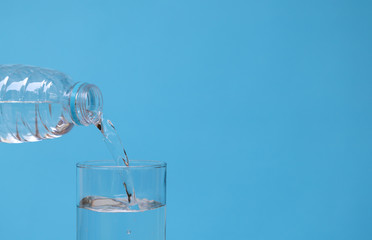 Pouring mineral drinking water from bottle into glass with blue background.