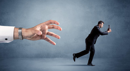 Young miniature businessman running from a big hand 