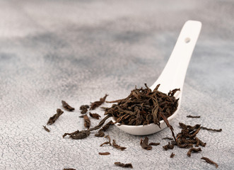 Fototapeta na wymiar Dry black tea in white ceramic spoon, isolated on grey