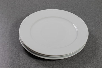 Weiße flache Teller aus Porzellan in einem Stapel auf einem grauen Tisch 