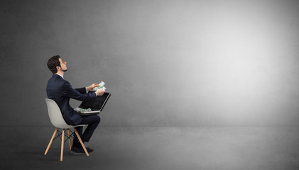 Businessman staying in an empty grey dark room with stuffs on his lap
