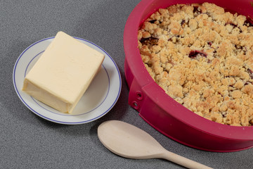 Frischer Pflaumenkuchen in Silikonbackform neben einem Stück Butter und einem Kochlöffel aus Holz