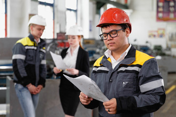 A young successful engineer with a drawing in his hands is standing in the territory of a modern factory.