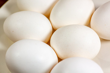 Eggs on a while plate sitting on the kitchen table waiting to be cracked
