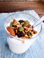 Healthy flavored yogurt in glass cup and spoon with cereal and granola isolated on the blue cloth background.