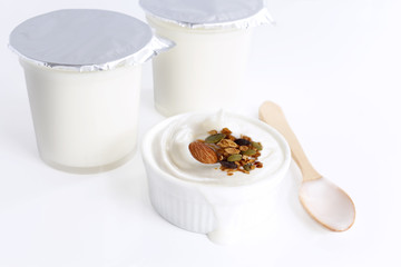 Healthy flavored yogurt in plastic cup and ceramic bowl with cereal and wooden spoon isolated on the white background. With copy space for your text.