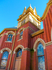 Beautiful church building in Greenville, TX, USA. Bright red brick wall of house with stained-glass windows and decor detail against blue sky.