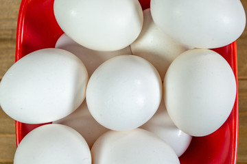 A group of eggs inside a deep red bowl waiting for the chef to use them in a meal