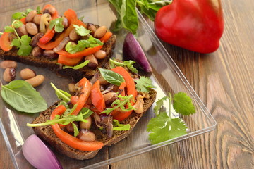 Rye bruschetta with beans, sweet peppers, arugula and red onion, copy space