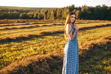 Beautiful young girl in a long sundress at sunset in the fields posing.