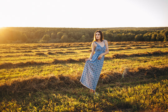 Beautiful young girl in a long sundress at sunset in the fields posing.