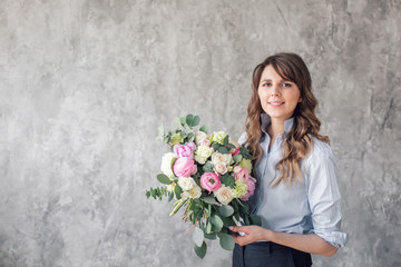 Young Woman looking at the camera, holds a luxurious bouquet in his hands. florist creating beautiful bouquet in flower shop. Girl assistant or owner in floral design studio.