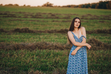 Beautiful young girl in a long sundress at sunset in the fields posing.